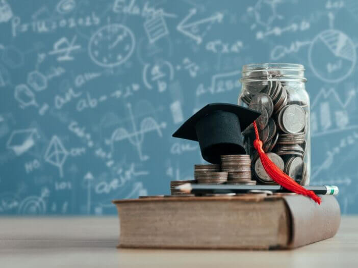 jar of money and grad cap sitting on top of a textbook