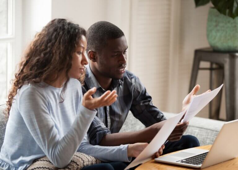 couple looking at a piece of paper and their computer having a serious discussion