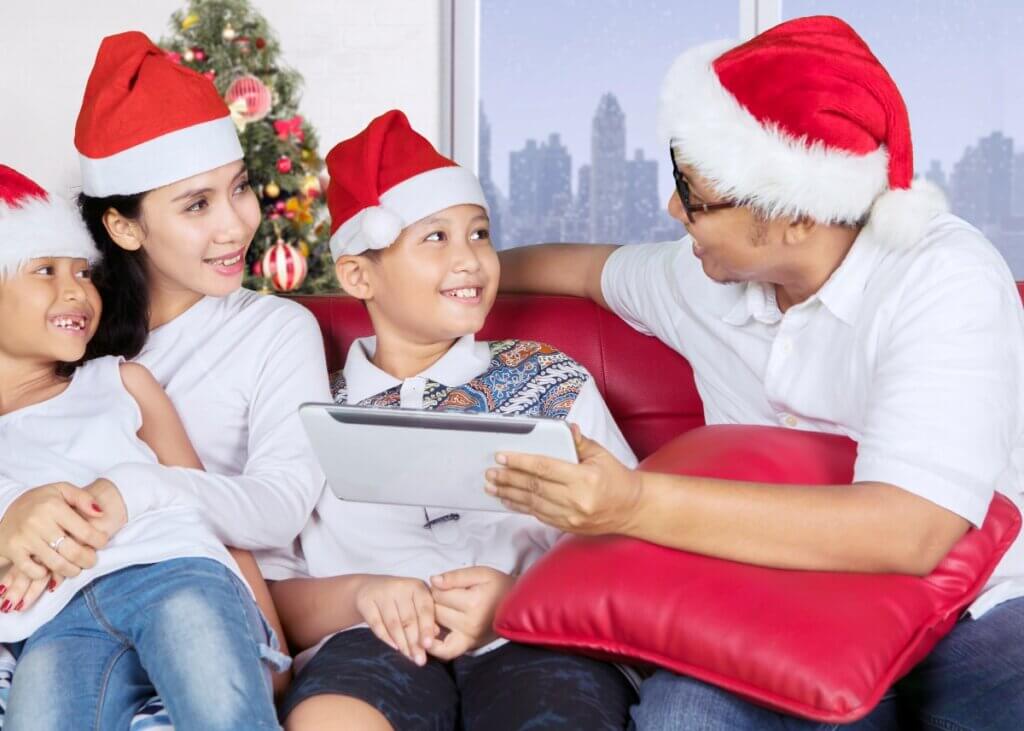 family of 4 sitting on the couch laughing with santa hats on