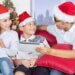 family of 4 sitting on the couch laughing with santa hats on