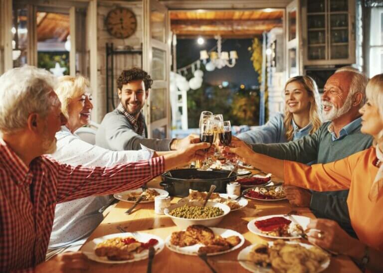 family around the thanksgiving table putting their glasses together cheersing