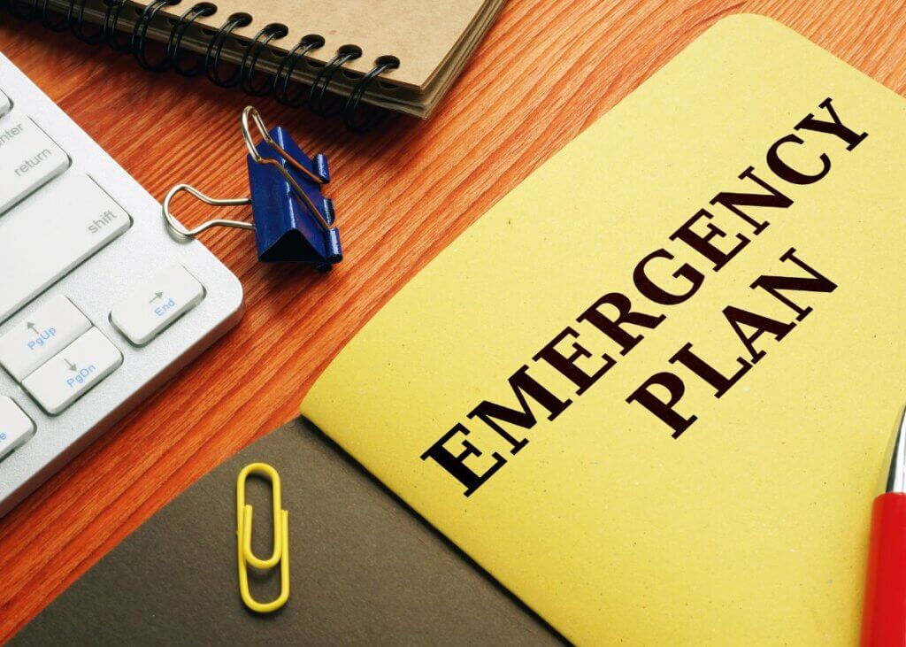 An image of a yellow emergency plan book on a desk with a keyboard and paper clips