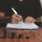 a guy paying off his debts filling out paperwork blurred in the background and there are a stack of coins focused in the image in front of him