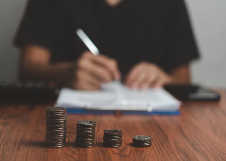 a guy paying off his debts filling out paperwork blurred in the background and there are a stack of coins focused in the image in front of him