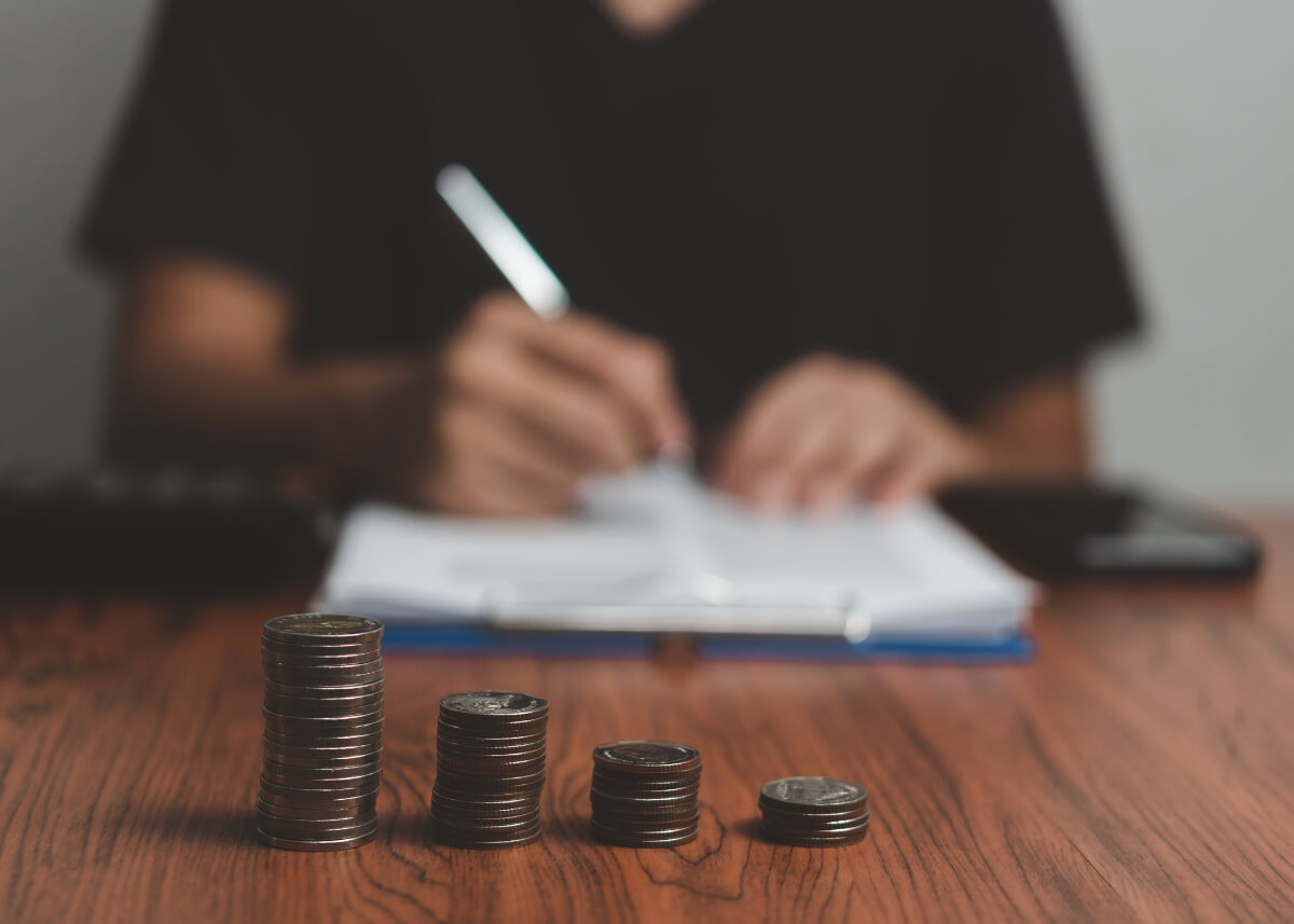 a guy paying off his debts filling out paperwork blurred in the background and there are a stack of coins focused in the image in front of him