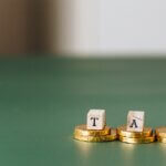 a picture of a stack of three golden coins and on top of each coin has a letter- that spells out tax