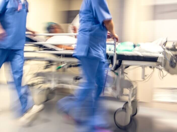 a picture of an emergency room bed being rushed by nurses with a patient lying in the bed. it is blurred and gives a chaotic and rushed feel