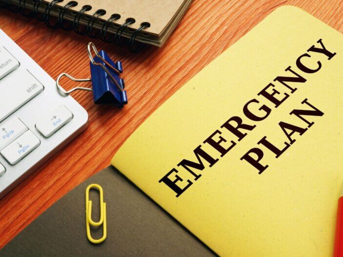 An image of a yellow emergency plan book on a desk with a keyboard and paper clips