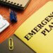 An image of a yellow emergency plan book on a desk with a keyboard and paper clips