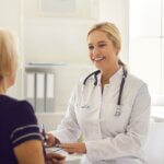 Doctor facing an older woman and writing down notes during a consultation.