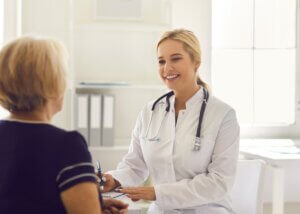 Doctor facing an older woman and writing down notes during a consultation.