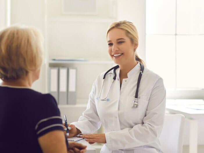 Doctor facing an older woman and writing down notes during a consultation.