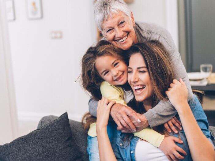 a grandma, a daughter, and granddaughter all hugging- showing the three generations and they are all laughing and smiling.