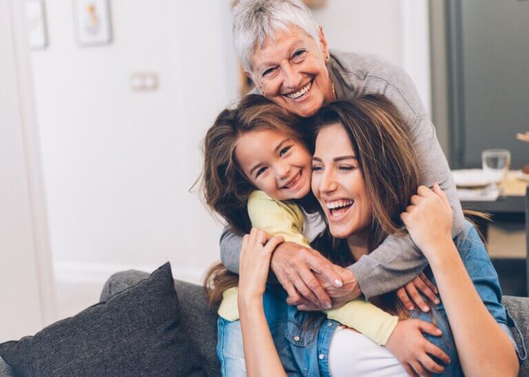 a grandma, a daughter, and granddaughter all hugging- showing the three generations and they are all laughing and smiling.