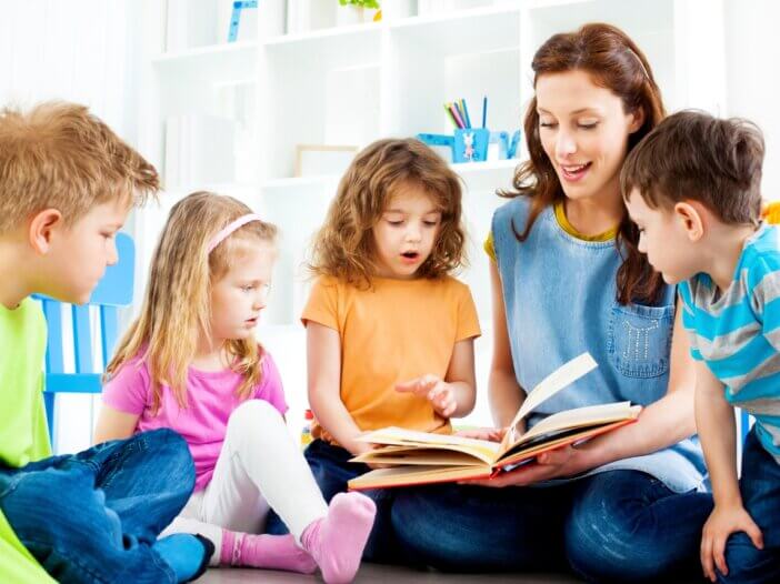 a mom with her four little kids with a book in her lap reading a story to them