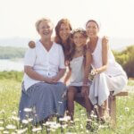 a picture of three generations- a grandma, a mom, and a kid. all in a grass field wearing white sitting down and smiling