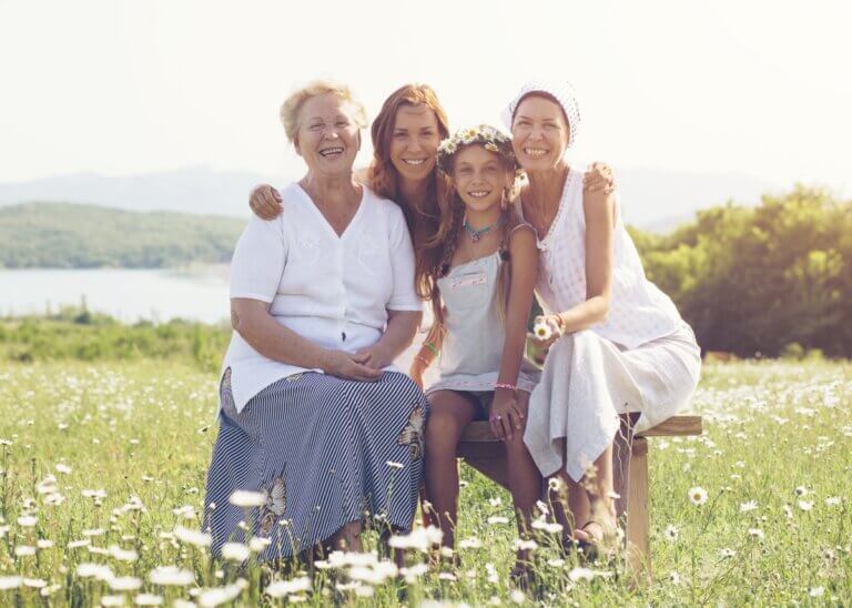 a picture of three generations- a grandma, a mom, and a kid. all in a grass field wearing white sitting down and smiling