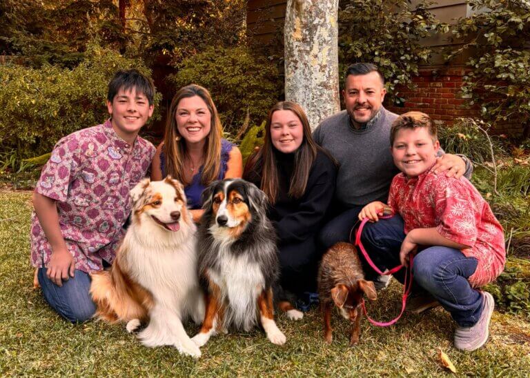 a picture of kevin and carolyn and their three kids with their two dogs. they are all huddled around each other smiling. showing how lucky they all are to have each other.