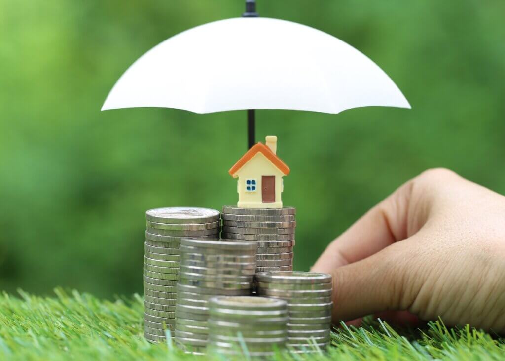 a little house on top of a stack of coins and an umbrella protecting these coins and house