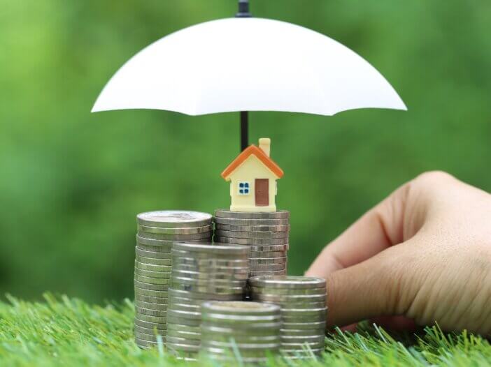 a little house on top of a stack of coins and an umbrella protecting these coins and house